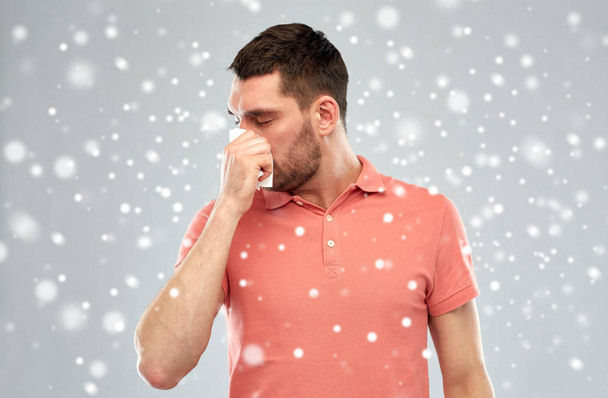sick man with paper wipe blowing nose over snow - Foto, afbeelding