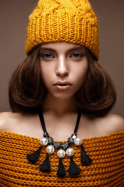 Beautiful girl in a knitted hat on her head and a necklace of pearls around her neck. The model with gentle make-up and gold lips. Beautiful face. - Foto, Bild