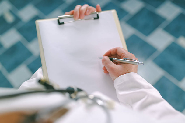 Female doctor in white uniform writing on clipboard paper - Zdjęcie, obraz