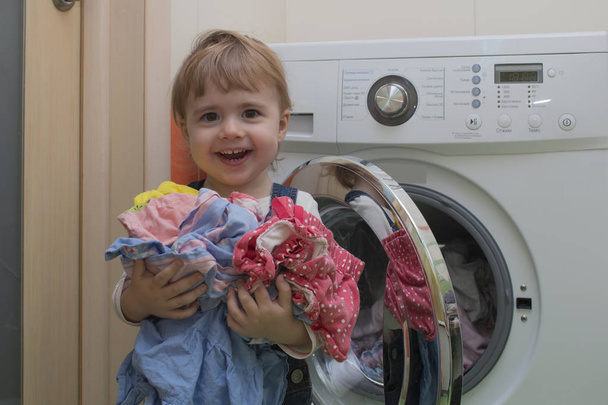 Joyeux mignon petite fille avec des vêtements faire la lessive à l'intérieur de la maison
 - Photo, image