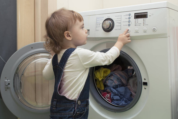 Küçük çocuk çamaşır makinesi başlar. Anneler yardımcı. 2 yaşında. - Fotoğraf, Görsel