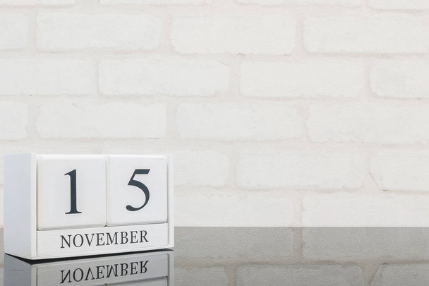 Closeup calendário de madeira branco com preto 15 Novembro de palavra sobre mesa de vidro preto e parede de tijolo branco texturizado fundo com espaço de cópia, foco seletivo no calendário
 - Foto, Imagem