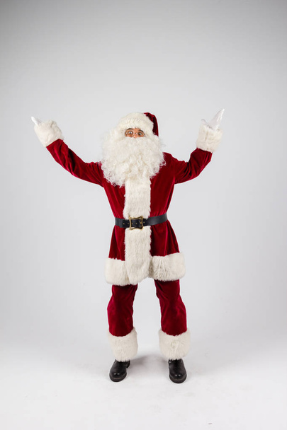 Santa Claus in eyeglasses and red costume throwing up hands on white background and looking into camera - Fotografie, Obrázek
