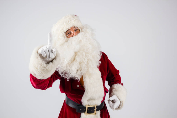 Santa Claus en gafas y traje rojo hacen un punto con las manos en el fondo blanco y mirando a la cámara
.  - Foto, imagen