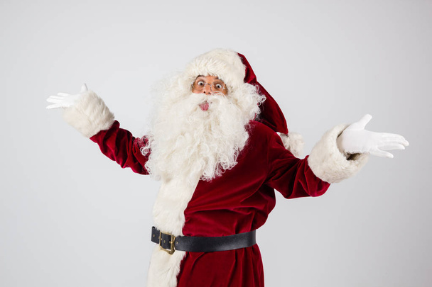 Santa Claus in eyeglasses and red costume throwing up hands on white background and looking into camera.  - Valokuva, kuva