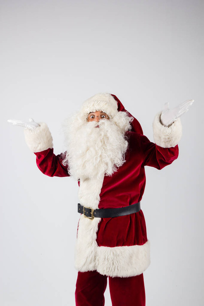 Santa Claus en gafas y traje rojo vomitando las manos sobre fondo blanco y mirando a la cámara
.  - Foto, Imagen