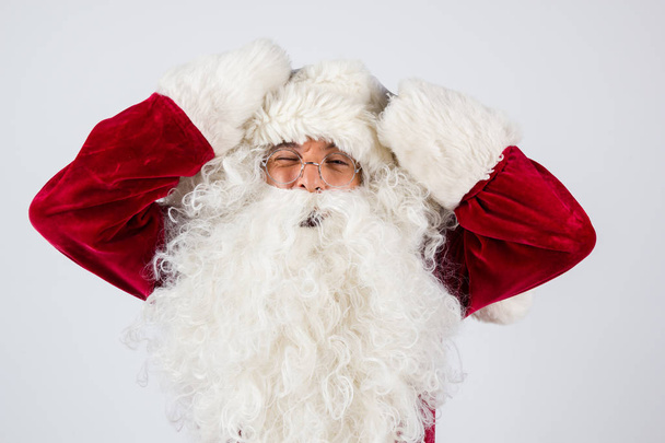 Weihnachtsmann in Brille und rotem Kostüm legt die Hände auf den Kopf vor weißem Hintergrund und blickt in die Kamera.  - Foto, Bild