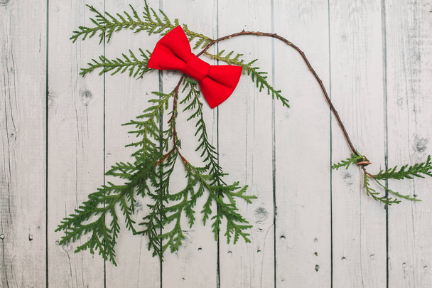 Рождественское украшение в винтажном тонизировании на белом деревянном фоне с красной бабочкой и еловой веткой. Рождественские украшения для деджина. Искусство с фактурой к празднику Нового 2017 года
 - Фото, изображение