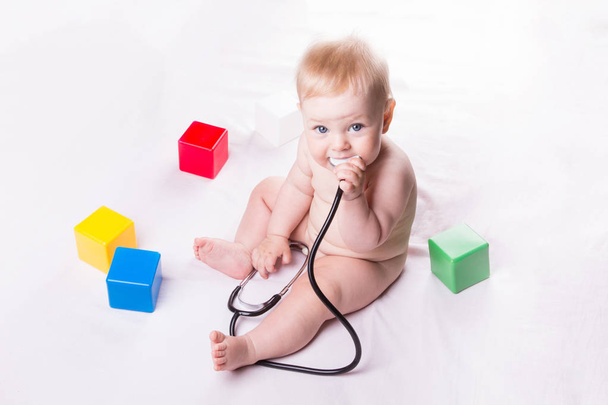 Baby sitting on the bed, playing with stethoscope. - Foto, Imagem
