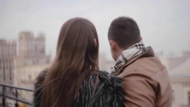 Back and side view of lovers on a roof enjoying the city view. They kiss, talk smile to each other. Cold foggy weather. - Filmagem, Vídeo