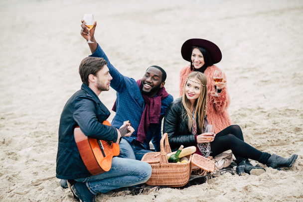 Счастливые молодые друзья с гитарой на пикнике
 - Фото, изображение