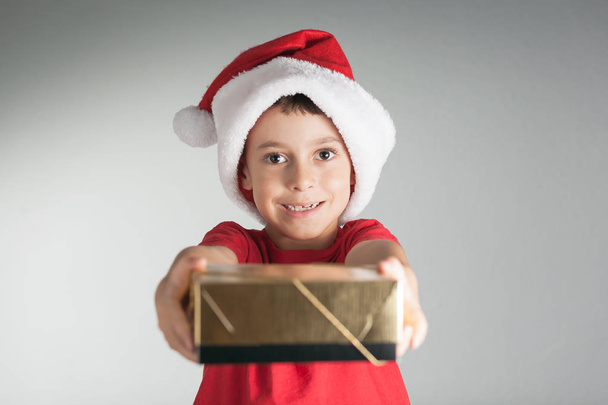 Smiling funny child in Santa red hat holding Christmas gift in hand. Christmas concept - Photo, Image