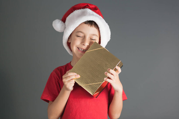 Smiling funny child in Santa red hat holding Christmas gift in hand. Christmas concept - Foto, Imagem