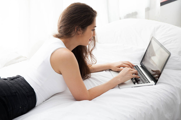 Beautiful woman laying down on white bed using laptop - Foto, Bild
