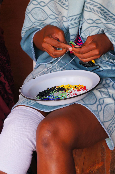 Mulher africana fazendo lembranças para vender na Villa Cultural Lesedi
 - Foto, Imagem