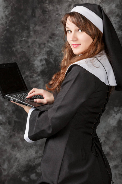 Η καθολική καλόγρια εργασίας και χρήση computer.young γυναίκα με ένα laptop σε σκούρο φόντο - Φωτογραφία, εικόνα