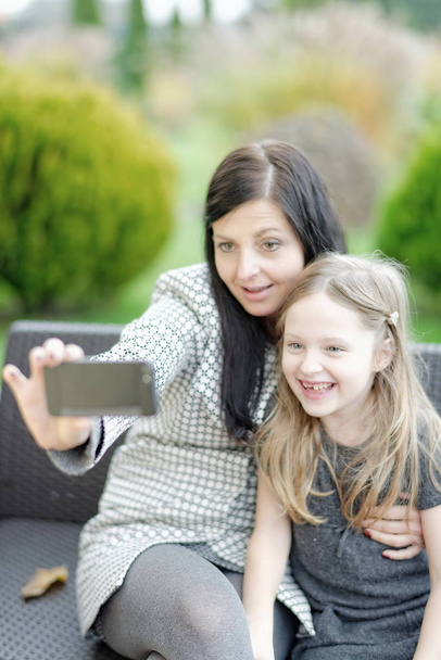 Mutter und Tochter sitzen in der Natur und sprechen Selfie  - Foto, Bild