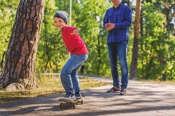 Carefree kid standing on skateboard near parent - Foto, imagen