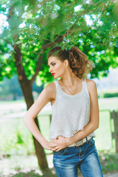 young woman outdoors in a white t-shirt and jeans, with bright makeup, red lips - Photo, image