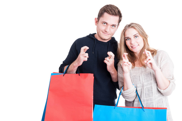 Couple holding shopping bags making fingers crossed gesture - 写真・画像