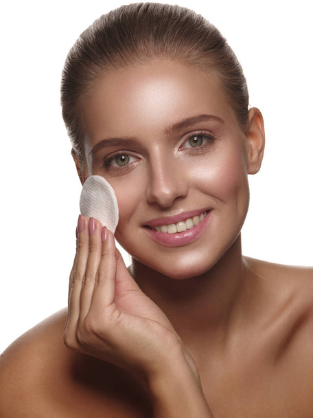 Portrait of a girl with pure and healthy glowing skin without makeup, who is doing daily cleansing procedures using a cotton pad after shower, wellness and spa, white isolated background - Valokuva, kuva