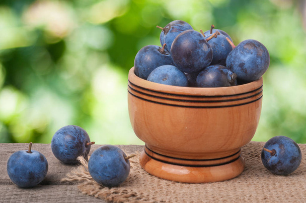 blackthorn berries in a wooden bowl on table with sacking and blurred background - Photo, Image
