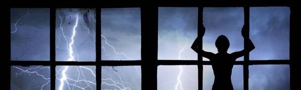 Sylwetka człowieka oglądania błyskawice, grzmoty, deszcz i burza przez rozbite okno opuszczony budynek - Zdjęcie, obraz