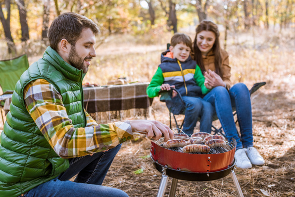Cheerful parents with son grilling sausages - Photo, Image