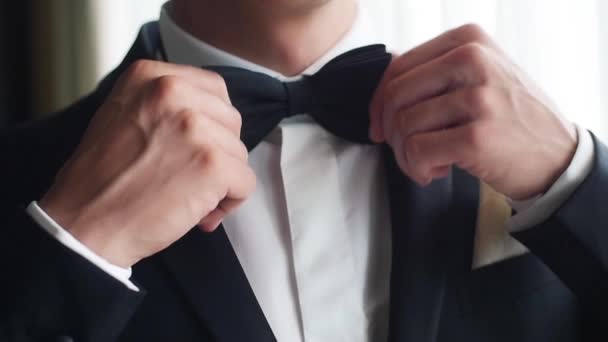 Ο άνθρωπος ρυθμίζει μαύρο παπιγιόν closeup αργή κίνηση. Αρσενικό χέρια σωστή παπιγιόν με άσπρο πουκάμισο φορούν κοστούμι προετοιμασία για το γάμο. Τζέντλεμαν μόδα τάσεις μόδας μοντέρνος επιχειρηματίας στολή κόμμα φωτεινή εικόνα - Πλάνα, βίντεο
