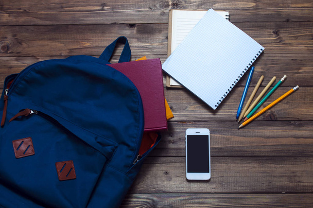 книги, синій рюкзак, канцелярські товари для навчання на дерев'яному тлі. мобільний телефон
. - Фото, зображення