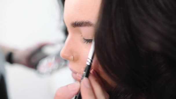 Make-up stylist maakt smokey eyes effect voor vrouw op fotoshoot, make-up voor mooie Kaukasische model, meisje komt naar beauty salon - Video