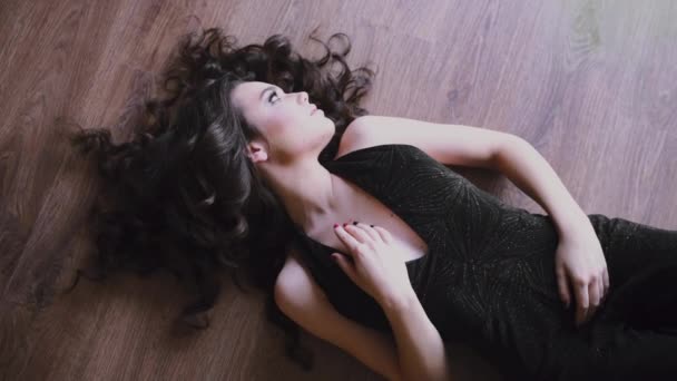 Seksowna kaukaski kobieta układa się na podłodze w strój wieczorowy, piękna dziewczyna z długimi włosami w stroju drażnić, ładna kobieta trzyma rękę na ozdoby - Materiał filmowy, wideo