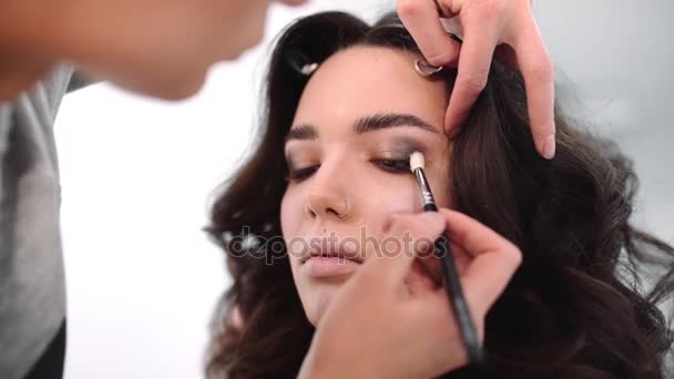 Make up stylist makes smokey eyes effect for woman at photo shoot, make up for beautiful caucasian model, girl comes to beauty fashion salon - Filmati, video