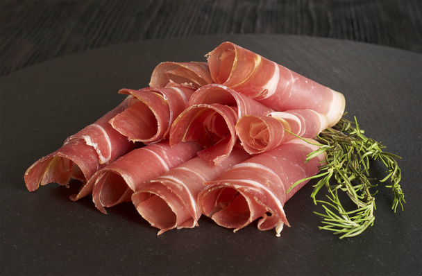 Gesneden Prosciutto-ham, houten achtergrond, rozemarijn - Foto, afbeelding