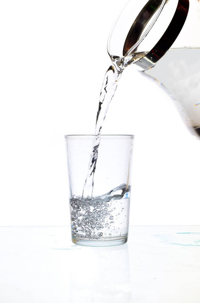 Наливаємо воду зі скляного глечика на білому тлі
 - Фото, зображення