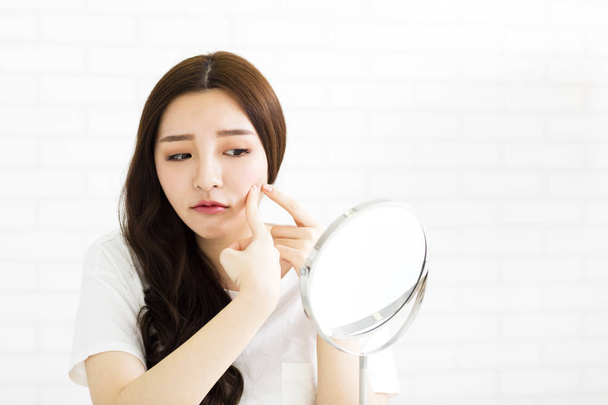 junge Frau drückt ihre Akne vor dem Spiegel zusammen - Foto, Bild