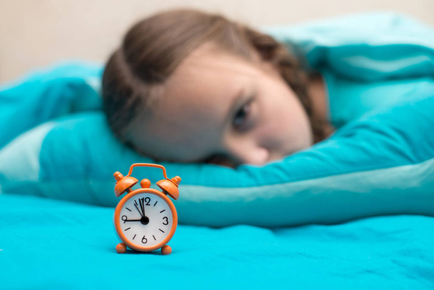 Teen girl lying in bed and holding an orange alarm clock - Foto, afbeelding