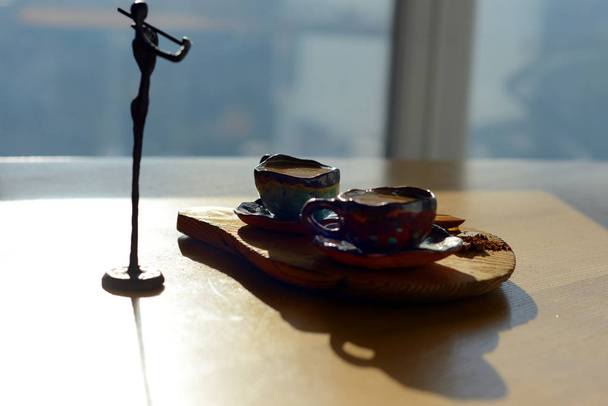 Фигура скрипача стоит рядом с деревянным стендом, на котором стоит чашка кофе и шоколад
. - Фото, изображение