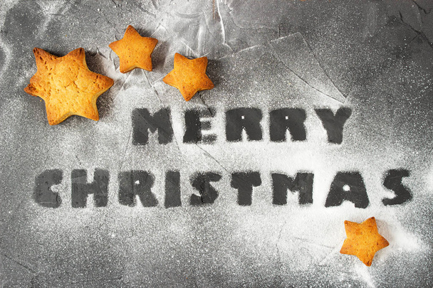 christmas background with baked gingerbread stars and words merry christmas made from powdered sugar. creative idea - Foto, afbeelding