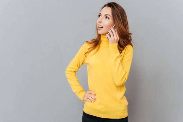 Woman in yellow sweater talking on phone and looking away - Zdjęcie, obraz