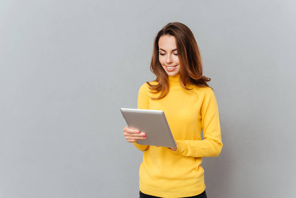 Smiling young woman in yellow sweater using tablet computer - Foto, afbeelding