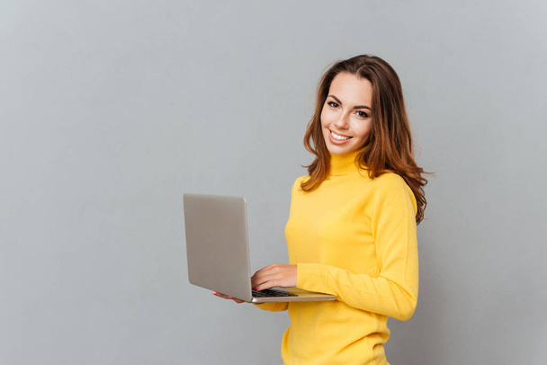 Smiling woman using laptop computer and looking at camera - Фото, изображение