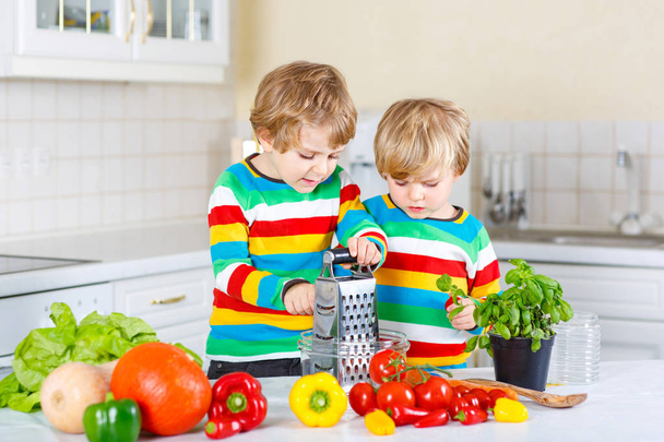 Kaksi pientä poikaa tekee salaattia vihanneksista
 - Valokuva, kuva