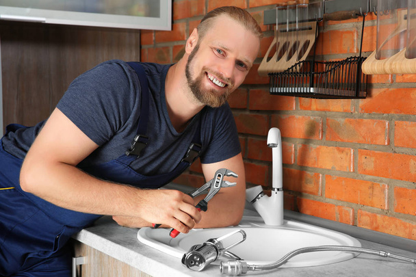 Handsome plumber replacing faucet in kitchen, close up view - Photo, Image