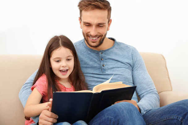 Father and daughter reading book on couch - 写真・画像
