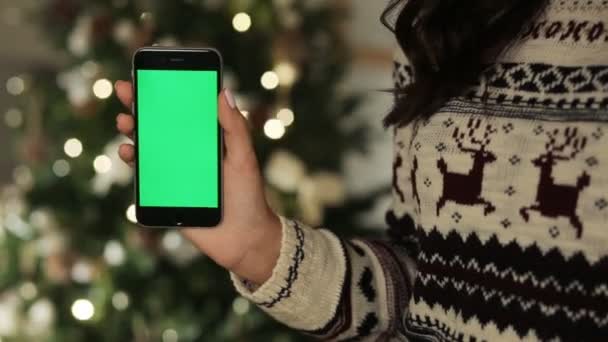Primer plano de las manos femeninas tocando el teléfono inteligente. Llave de croma de pantalla verde. De cerca. Movimiento de rastreo. con fondo borroso decoración de Navidad
 - Metraje, vídeo