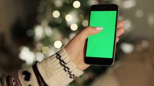 Γκρο πλαν του θηλυκού χέρια αγγίζει του smartphone. Πράσινη οθόνη Chroma Key. Κοντινό πλάνο. Παρακολούθηση κίνησης. με Θάμπωμα φόντου διακόσμηση Χριστουγέννων - Πλάνα, βίντεο