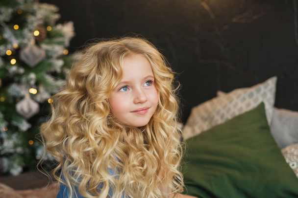Portrait of pretty blonde little girl smiles and looks side on a bed in Christmas time - Foto, Imagem