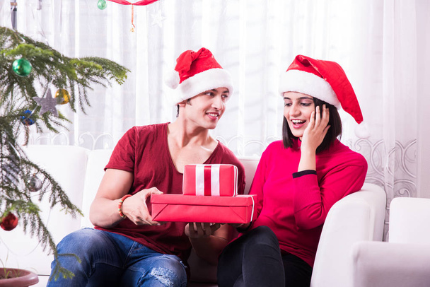 Καλά Χριστούγεννα. Νεαρό ζευγάρι ινδικές ή ασιατικές γιορτάζει τα Χριστούγεννα στο σπίτι με έκπληξη κουτιά δώρων - Φωτογραφία, εικόνα