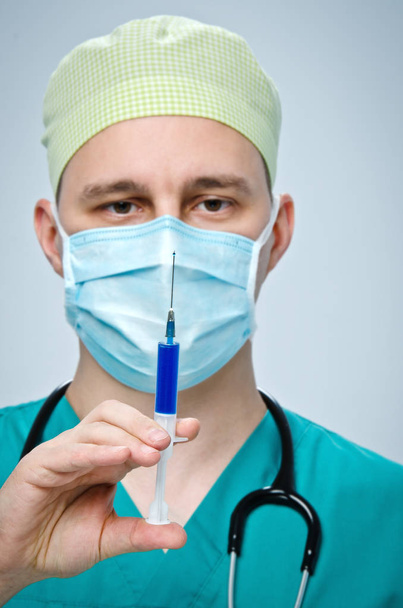 El médico con un sombrero verde y una máscara azul sosteniendo una jeringa con medicamento
. - Foto, Imagen